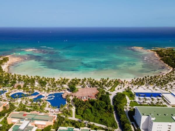 Aerial view of a tropical resort with turquoise waters, palm trees, and swimming pools along the Caribbean coastline.