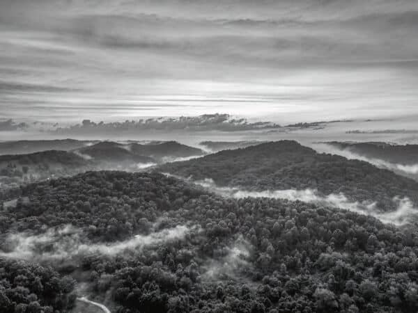 Black and white aerial view of misty mountains with fog and a dramatic sky, capturing the serene beauty of the Smoky Mountains.